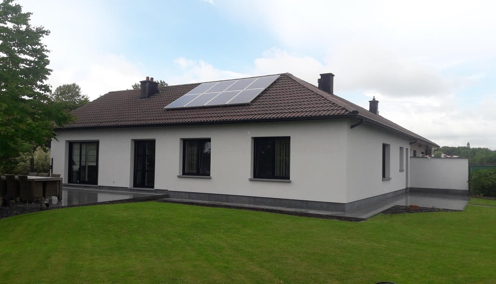 Gepleisterde woning met zonnepanelen op het dak en een gazon ervoor
